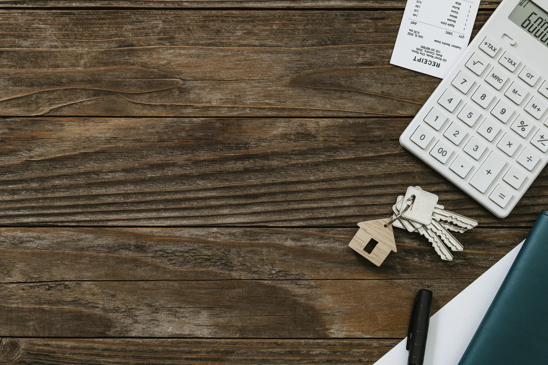 Calculator, house keys with a house-shaped keychain, receipt and folder on a wooden table