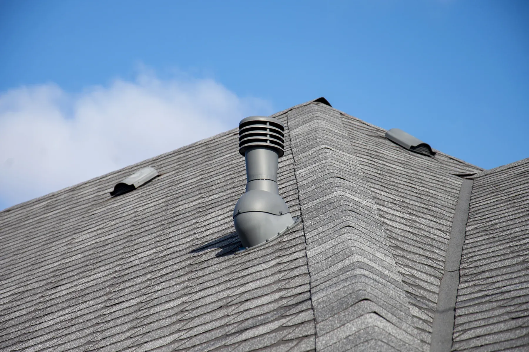Gray asphalt shingle roof with a round exhaust vent, low-profile vents and hip and ridge cap shingles