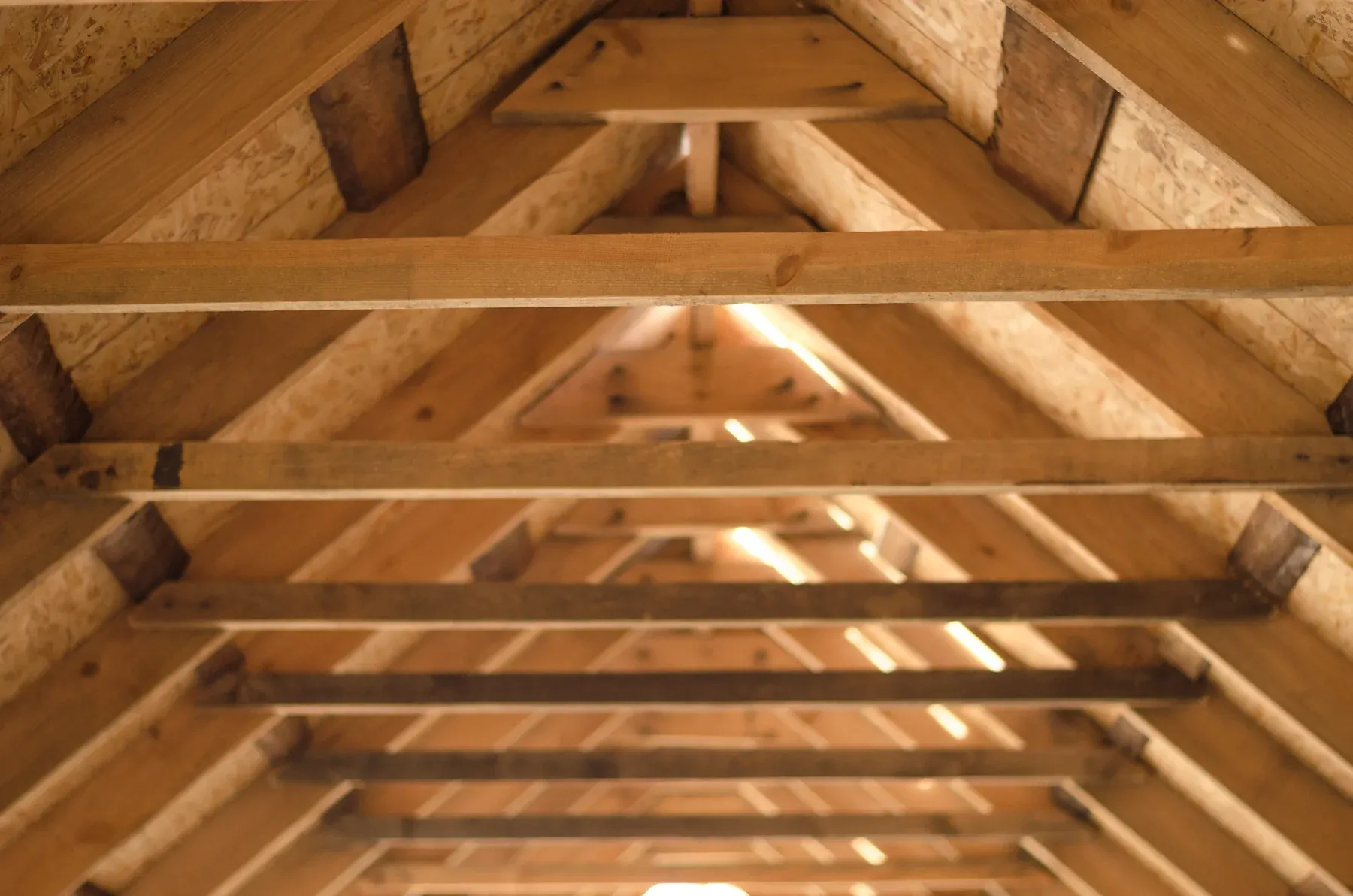 Unfinished attic with wood rafters, collar ties and OSB roof sheathing, daylight at the far end