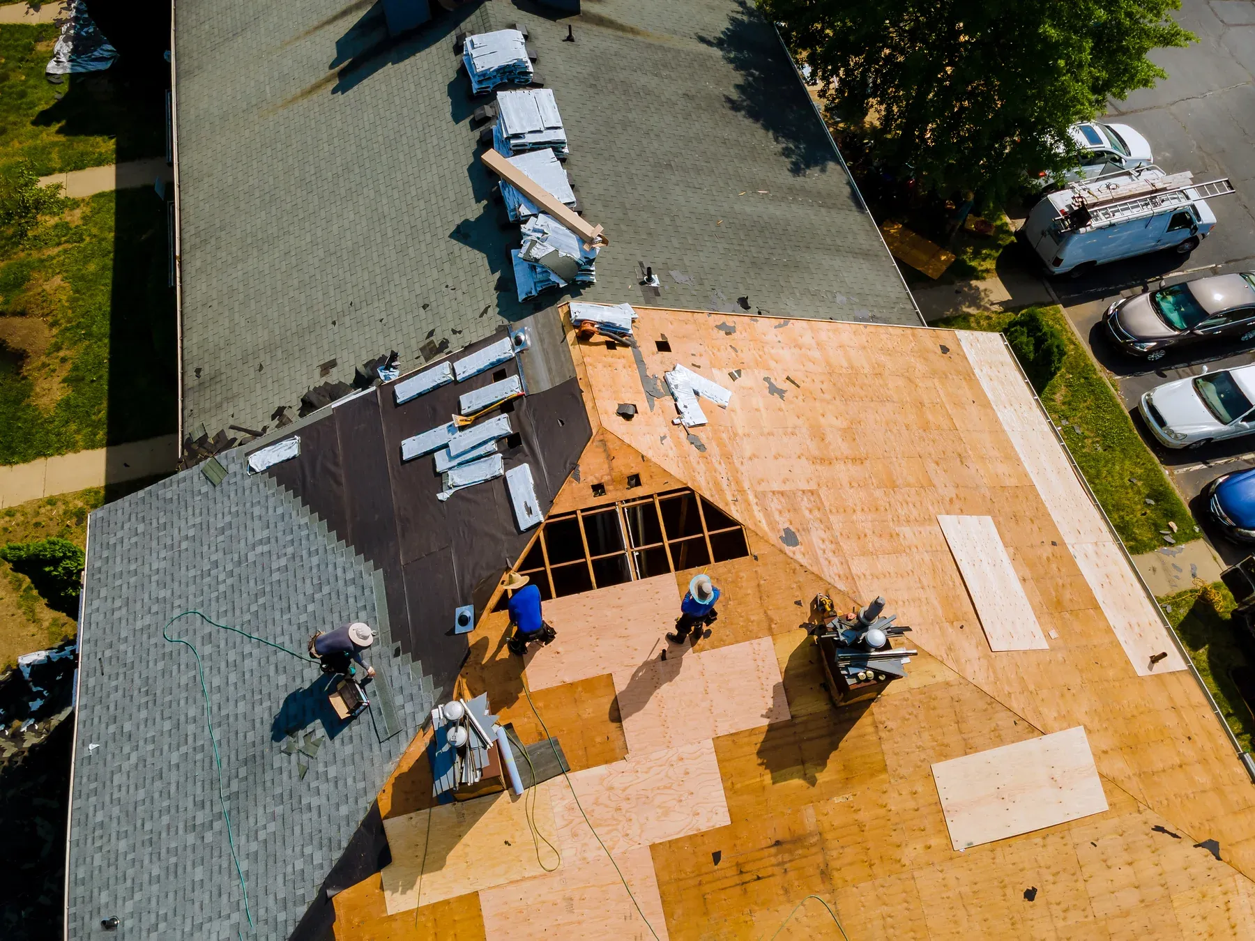 Aerial view of a roof replacement with new decking patches, underlayment and shingle bundles staged