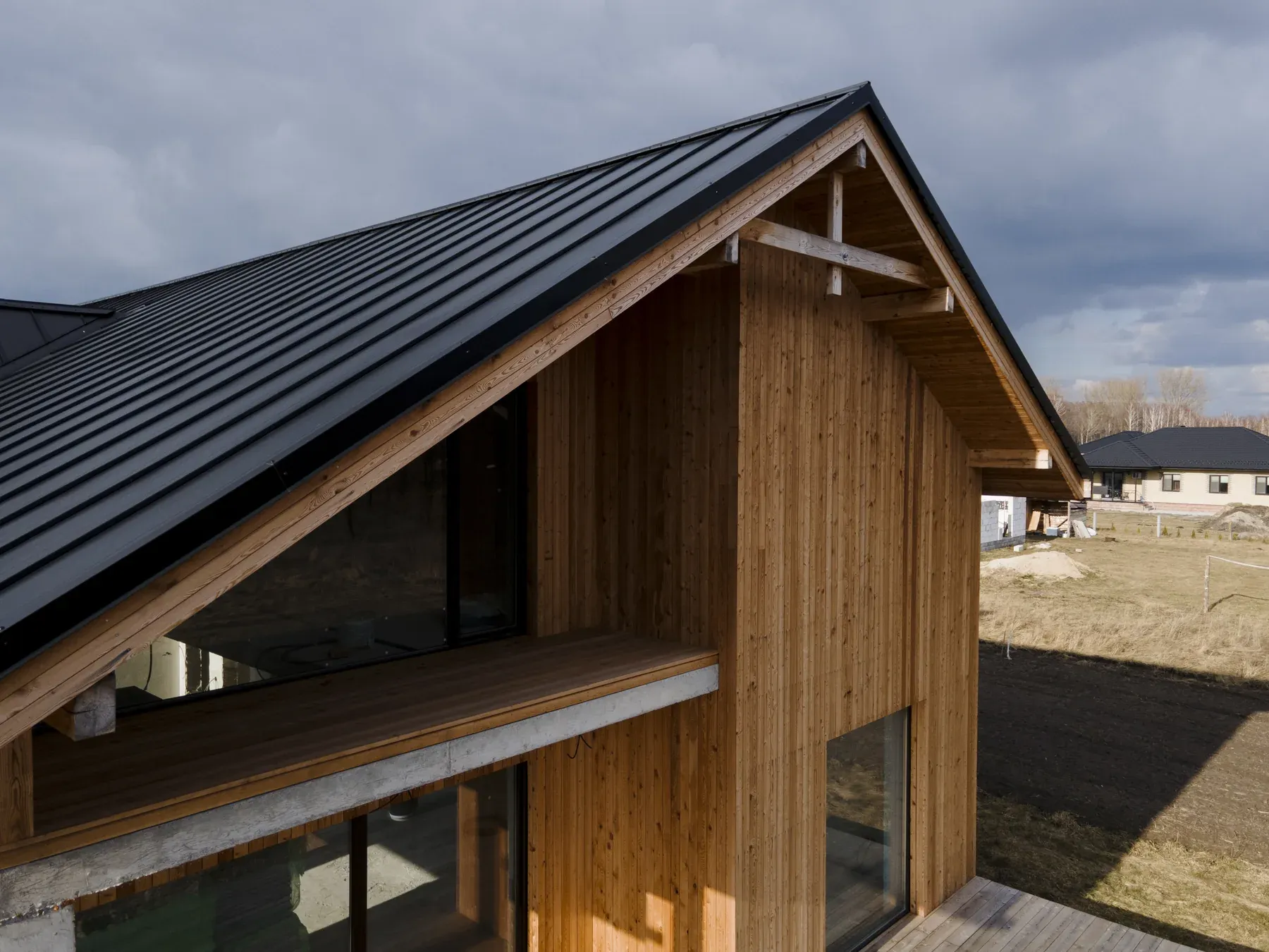 Modern wood-sided house with a dark standing-seam metal roof under a cloudy sky