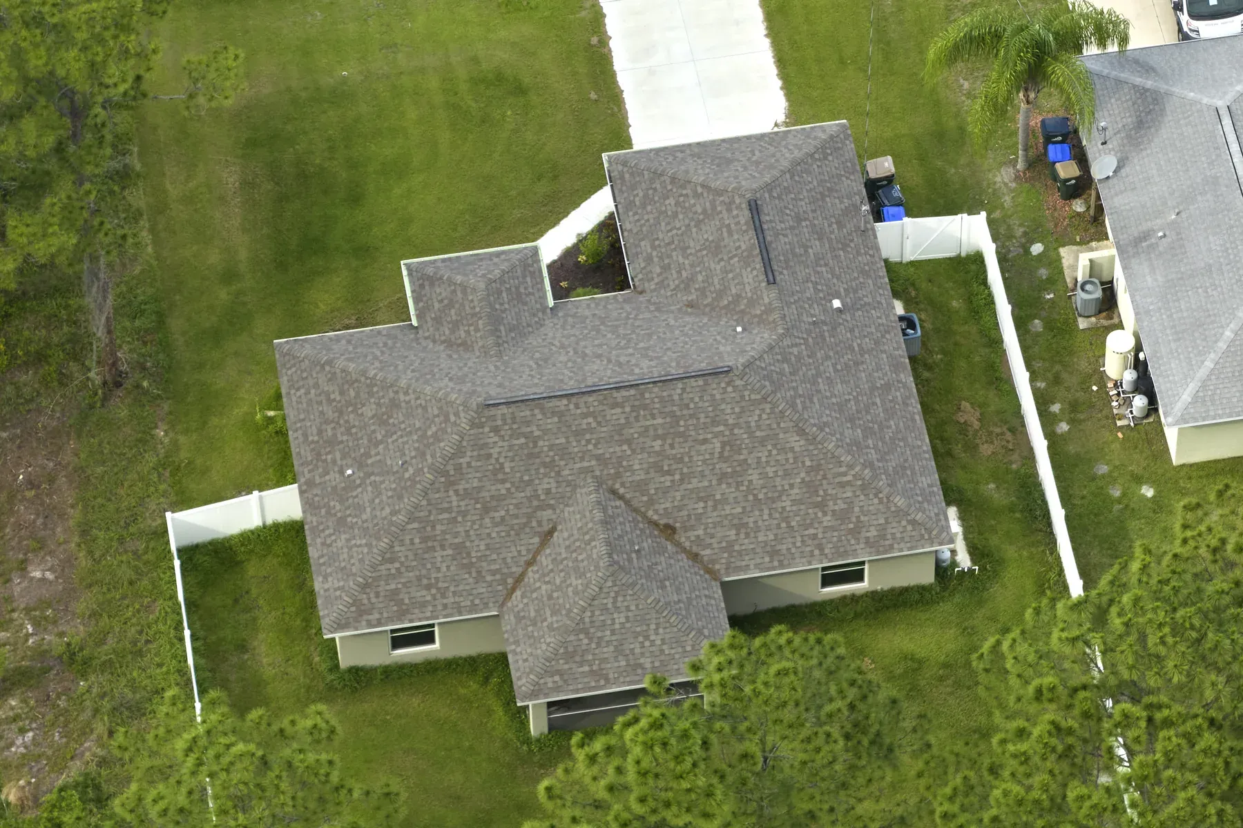 Aerial view of a single-story house with a gray architectural asphalt shingle hip roof beside a green lawn