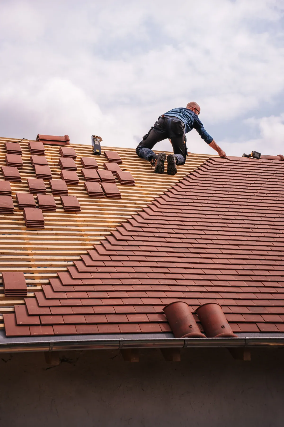A roofer working on a pitched residential roof beneath clouds