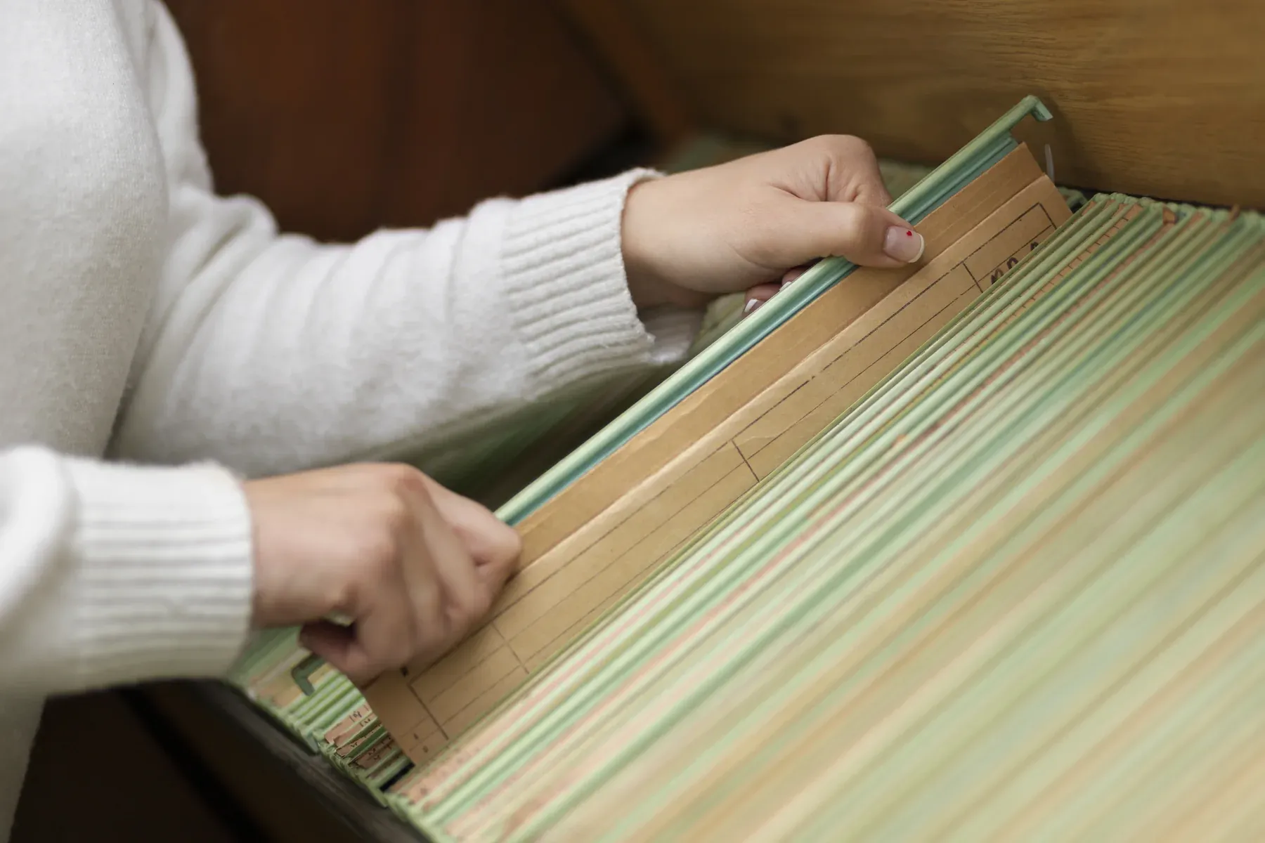 Hands sorting through hanging file folders in an open drawer to store paperwork