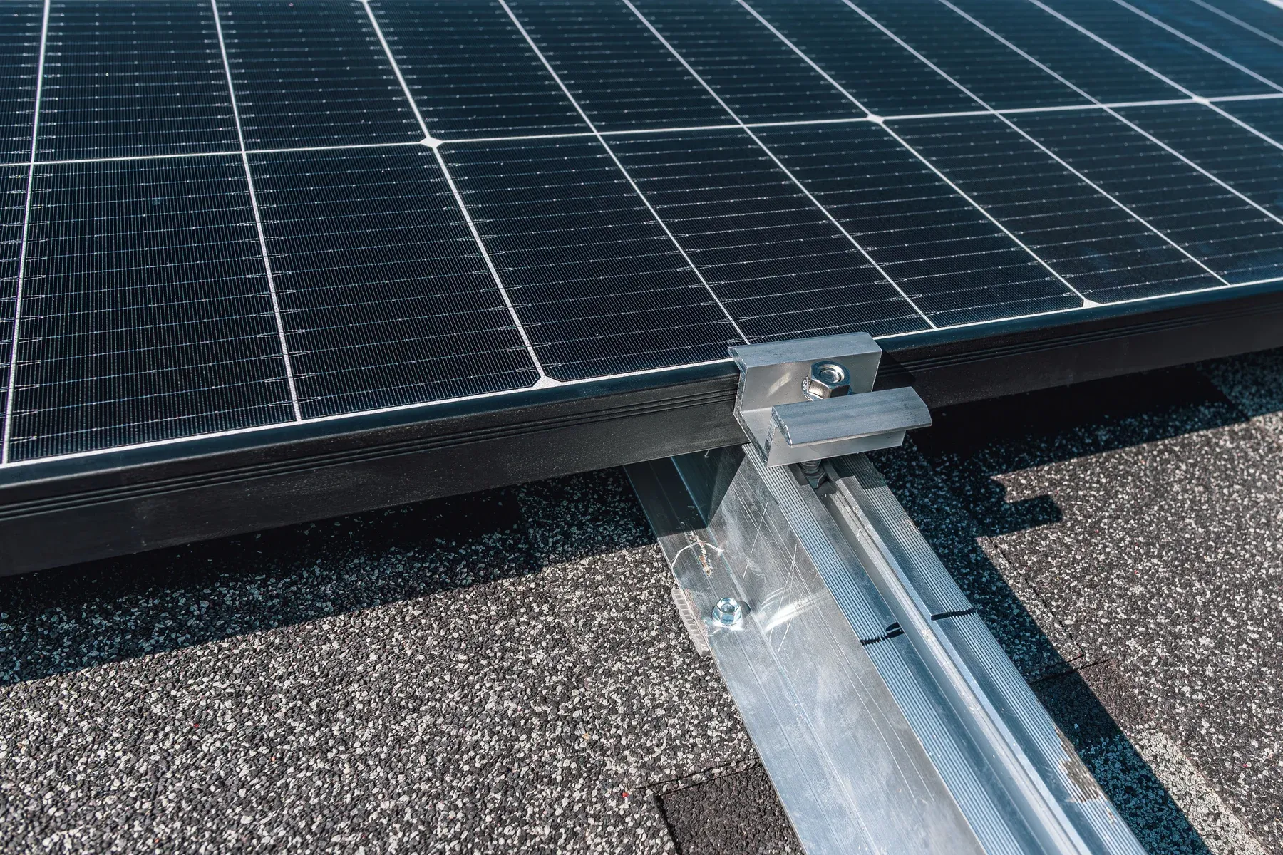 Close-up of an aluminum mounting rail and clamp holding a solar panel above a roof