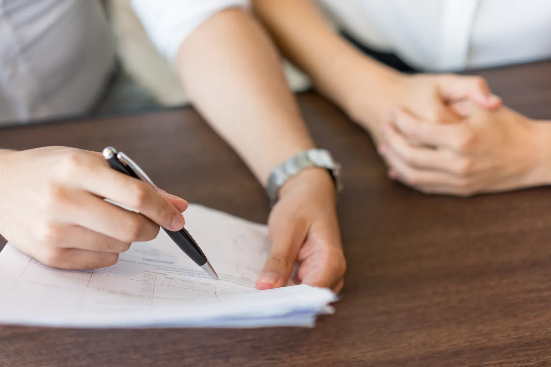 Two people at a table, one pointing with a pen to a line on a printed contract
