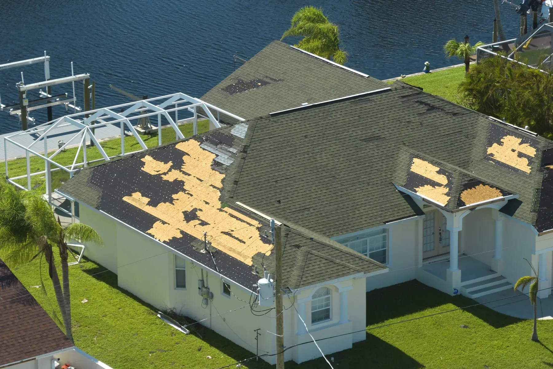 Aerial view of a storm-damaged house with large patches of missing shingles and bare roof decking