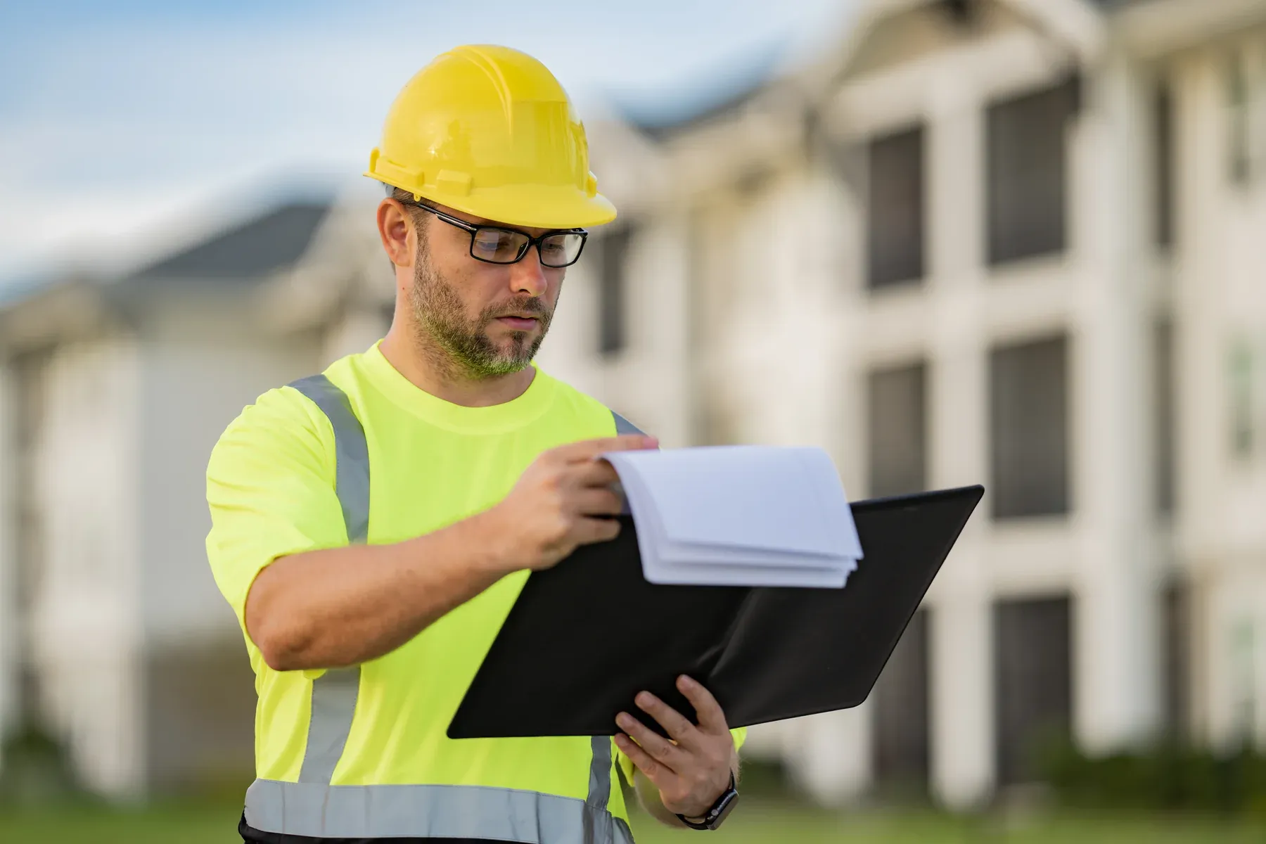 Inspector in a yellow hard hat and safety vest reviewing notes on a clipboard outdoors